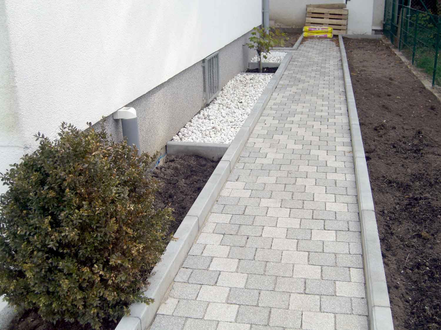 MDS-bautenschutz-bausanierung-frankurt-Kellersanierung-Ducariu-in-Frankfurt-gepflasterter-Weg Neu gepflasterter Weg entlang eines Gebäudes mit Randsteinen, Kiesbeet und vorbereiteten Pflanzflächen – Teil einer Außenanlagen- oder Kellersanierung.