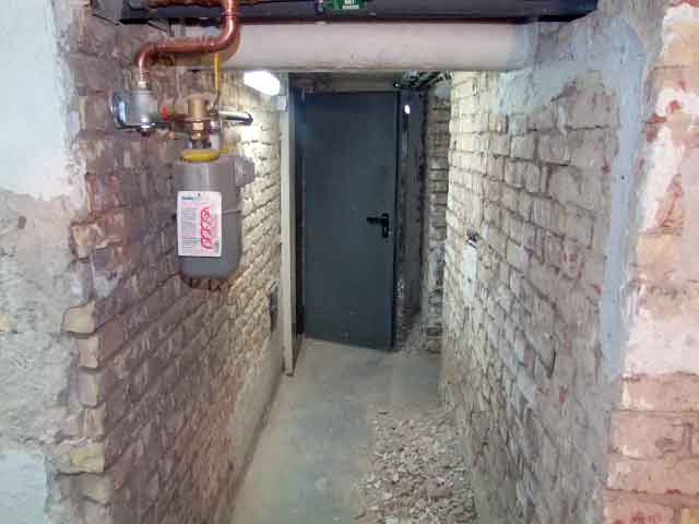 Feuchter, unrenovierter Kellerflur mit freiliegendem Mauerwerk und Rohrleitungen – typischer Zustand vor einer Kellersanierung.