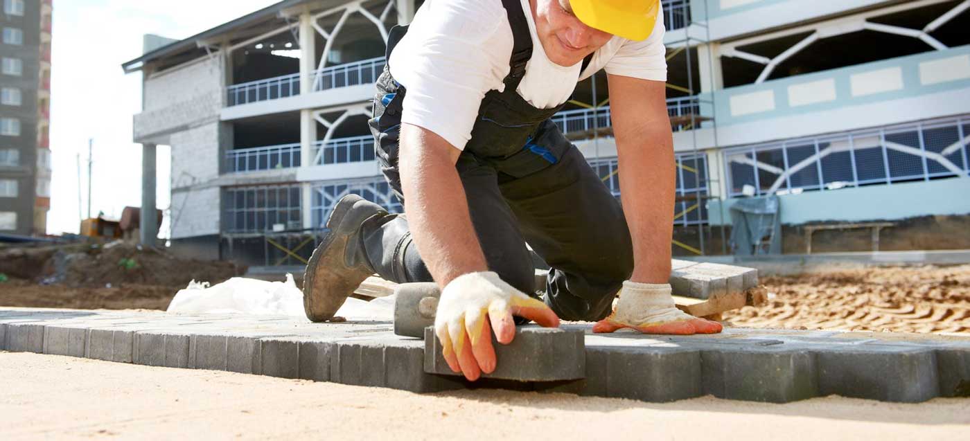 Bauarbeiter mit gelbem Helm verlegt Pflastersteine auf einer Baustelle – präzises Arbeiten beim Wegebau oder der Flächenbefestigung.