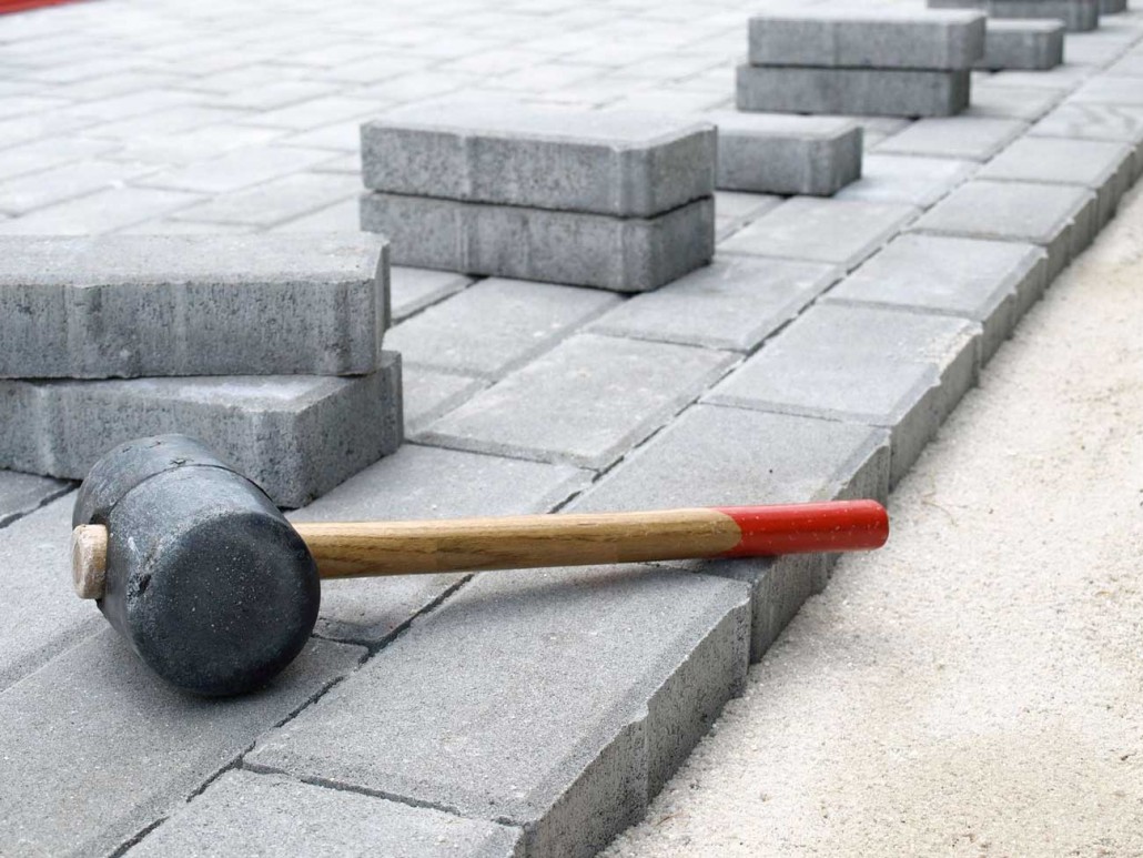 MDS-bautenschutz-bausanierung-frankurt-Plasterarbeiten-2 Verlegte Pflastersteine mit Gummihammer auf Sandbett – Vorbereitung und Ausrichtung beim Pflastern einer neuen Fläche.