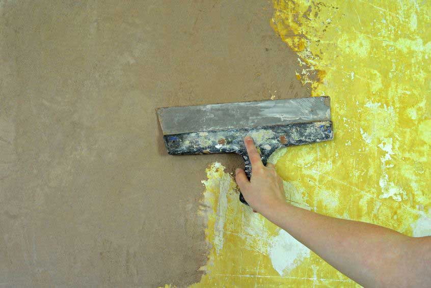 MDS-bautenschutz-bausanierung-frankurt-Risssanierung Hand mit Spachtel trägt Putz auf beschädigte Wand auf – Sanierungsmaßnahme zur Ausbesserung von Rissen oder alten Anstrichen.