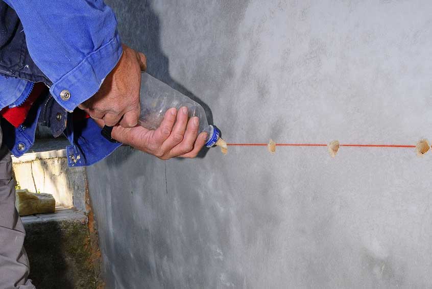 Facharbeiter befüllt Bohrlöcher in Betonwand mit Flüssigkeit – Vorbereitung zur Injektionsabdichtung oder Rissverpressung im Mauerwerk.