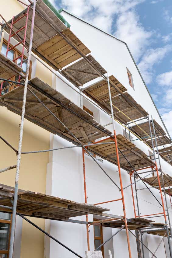 MDS-bautenschutz-bausanierung-frankurt-waermedaemmung-haus-1 Mehrstöckiges Baugerüst an einer frisch verputzten Fassade – Außenwandarbeiten im Rahmen einer energetischen Sanierung oder Wärmedämmung.